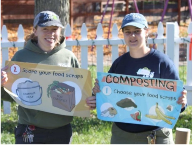 Educators Tara (left) and Emily (right) hold up informational decals to be installed on a compost tumbler